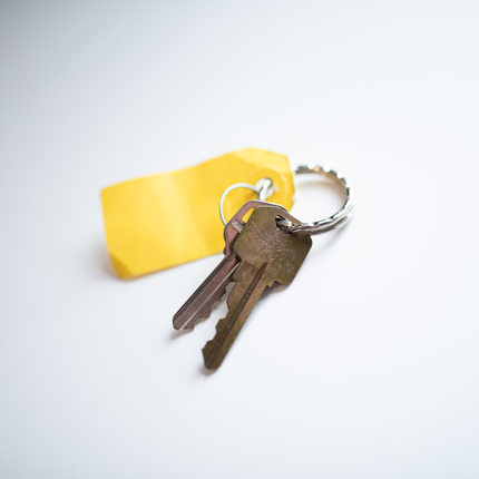 Par de llaves color café con una etiqueta amarilla puestas en un fondo blanco