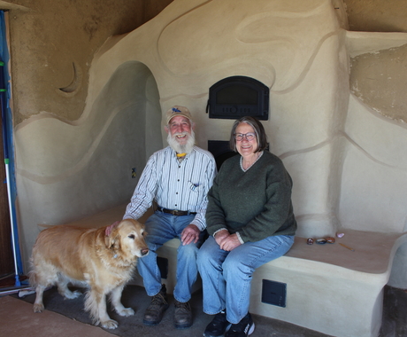 Man and woman sitting on a clay fireplace with a golden dog standing in front of them
