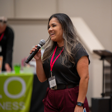 A Latina Woman with a black shirt smiling and talking into a microphone