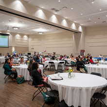 A room with white cloth covered tables, full of women sitting at the tables