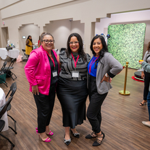 Tres mujeres posando para la cámara, en una sala de conferencias.