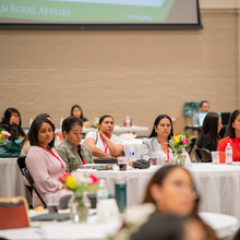 Un primer plano de una mesa con cinco mujeres latinas observando a un orador