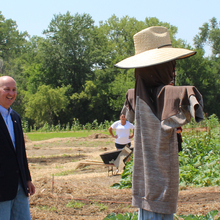 Two men looking at a high school student who placed a hat on a scarecrow