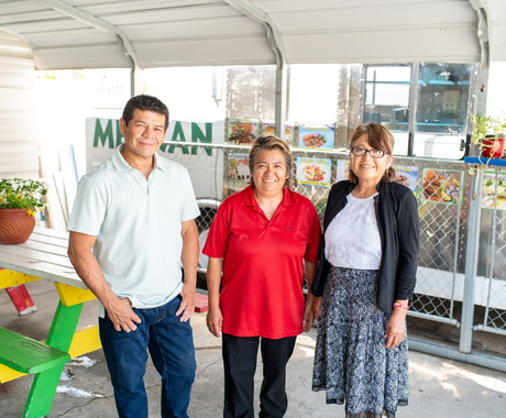 Tres personas de mediana edad, un hombre y dos mujeres, de pie frente a su camión de comida y al área cubierta para comer, sonriendo a la cámara.