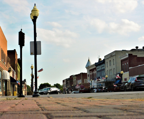 Community Main Street with buildings, light poles with American flats attached, and cars on both sides