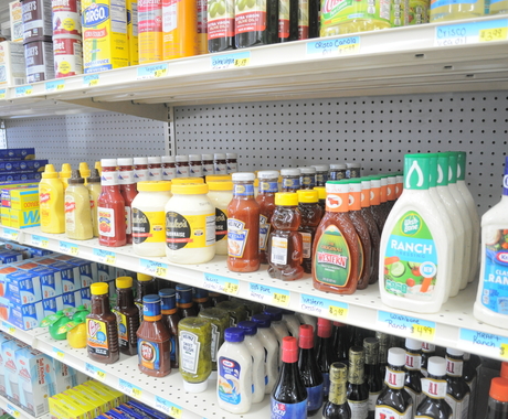 Estantes de comida en una tienda de comestibles de un pueblo pequeño. En primer plano, salsa ranch, ketchup, mayonesa, miel y, en el extremo izquierdo, papel de aluminio y bolsas de plástico.