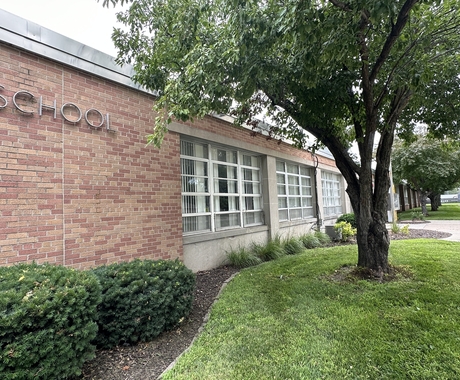 A school building with tree and green grass in the foreground