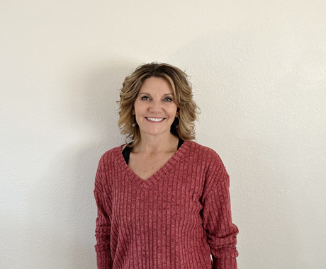 Woman with shoulder length hair wearing a pink v-neck sweater smiles at the camera