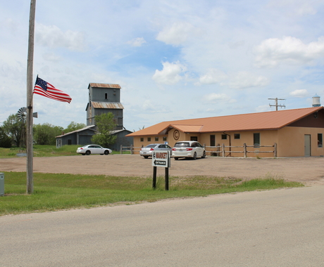 A one-story building with a sign out front that says "market." An American flag hangs from a light post, and in the background is a grain elevator.