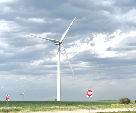 Wind turbine white in color sitting in a rural field off a road