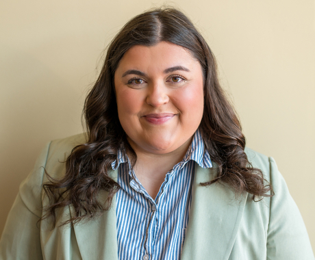 Woman with brown hair wearing a light colored blazer and blue striped shirt