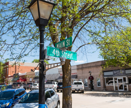 An artistic photo of a street sign that says Main St. and 4th Street with business buildings behind and cars parked on each side of the road