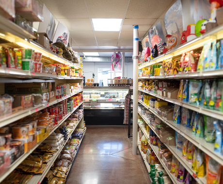 Aisle at a locally owned grocery store with shelves of food products on both sides of the aisle, and a meat counter at the front