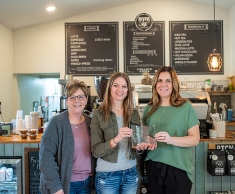 Tres dones blanques en una cafeteria es toman una foto amb un premi en mà