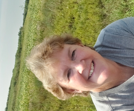 Mujer con cabello corto y rubio, sonriendo a la cámara, con una pradera detrás de ella.