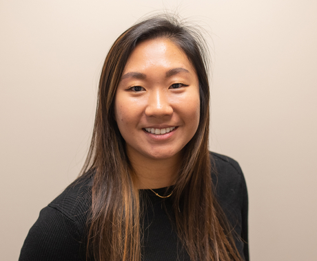 Asian woman with long dark hair smiling, looking directly at the camera, wearing a long sleeved black sweater