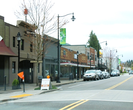 Store buildings on the left with cars parked along a main street.