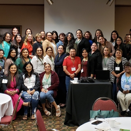 Un grupo de personas vestidas de manera informal, sentadas y de pie en 4 filas en una conferencia