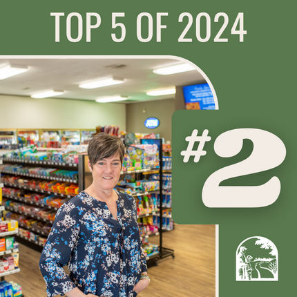 Graphic that says "Top 5 of 2024 #2" and photo: White woman with short brown hair wearing a dark flowered long sleeve top stands in the middle of a convenience store with lights above and products around her