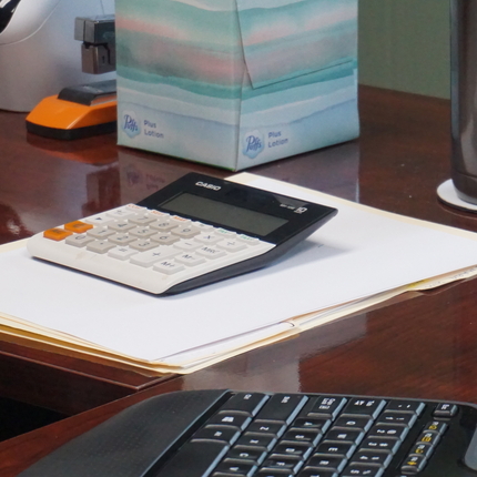 Una calculadora se encuentra arriba de un escritorio de madera junto a unos papeles en blanco y un teclado de computadora