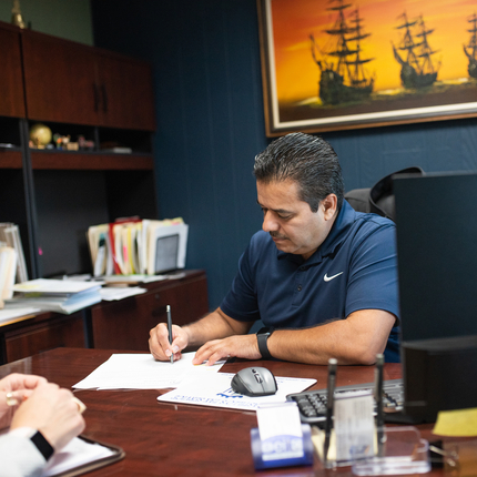 Un hombre con camisa azul sentado atrás de un escritorio firma documentos