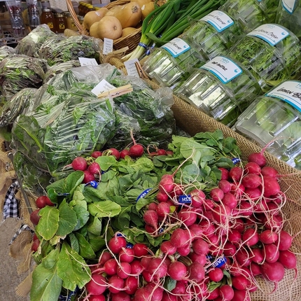 Verduras verdes, algunas envasadas y otras no, y rábanos se encuentran en una mesa de exhibición en una tienda de comestibles.