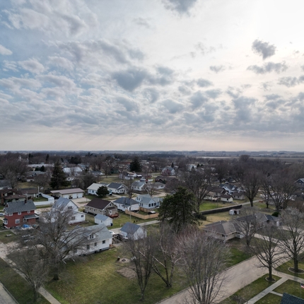 A drone shot of a rural community, with no leaves on the trees, and the grass turning green