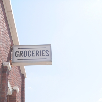 Mostly blue sky, at the left of the picture is a brick building with a white sign. In black lettering it says "groceries"