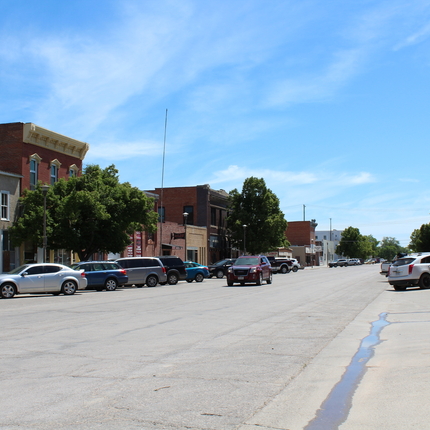 Small town main street with brick two-story buildings on each side and cars parked on either side.