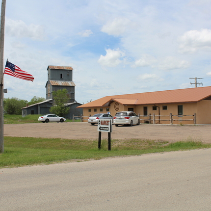 A one-story building with a sign out front that says "market." An American flag hangs from a light post, and in the background is a grain elevator.