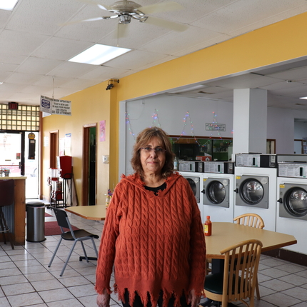 Dona llatina amb ulleres i una sudadera de manga larga color naranja per al centre d'un negoci de lavandería amb rentadores i taules amb sillas per altres