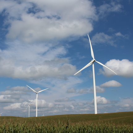 Wind turbines sit in a farm field with cloudy blue skies above.