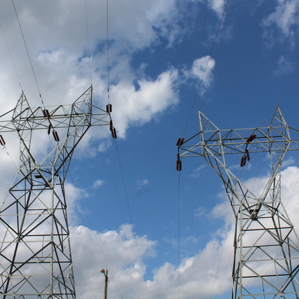 Looking up at transmission towers under a cloudy blue sky