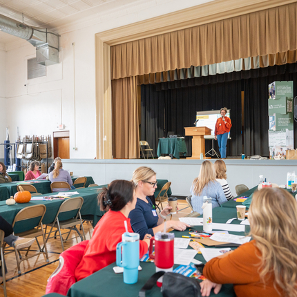 Local Foods Summit group photo. Speaker on a stage with people listening at tables below.