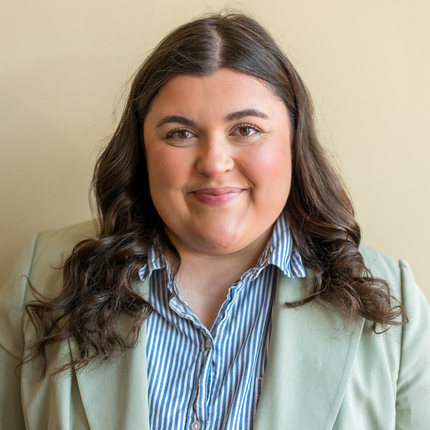 Woman with brown hair wearing a light colored blazer and blue striped shirt