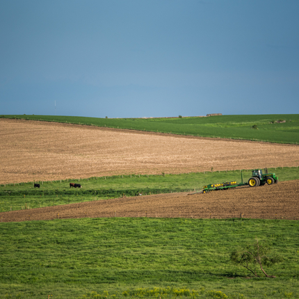 A farm field with a tractor planting crops in the distance