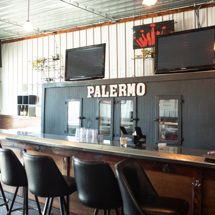 Un bar amb tamborets davant, amb "Palermo" a la paret, amb dos televisors apagats a la paret a sobre de la paraula