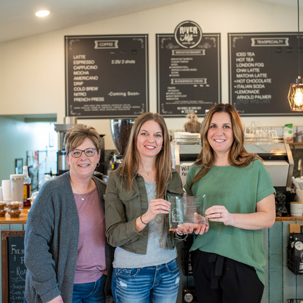 Three white females in a coffee shop holding an award