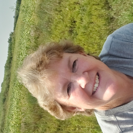 Mujer con cabello corto y rubio, sonriendo a la cámara, con una pradera detrás de ella.