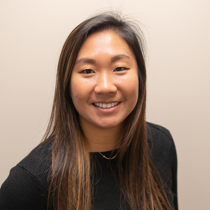 Asian woman with long dark hair smiling, looking directly at the camera, wearing a long sleeved black sweater