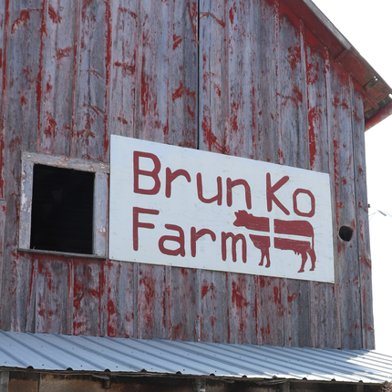 Masia amb un rètol que diu Brunk Ko Farm i un disseny de vaca en vermell.