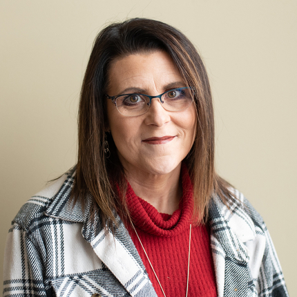 Woman wearing glasses in a white and black plaid blazer with a red shirt underneath poses for a picture