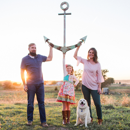 Retrat familiar d'un home, dona, filla i gos. Tots toquen una àncora en una pastura.