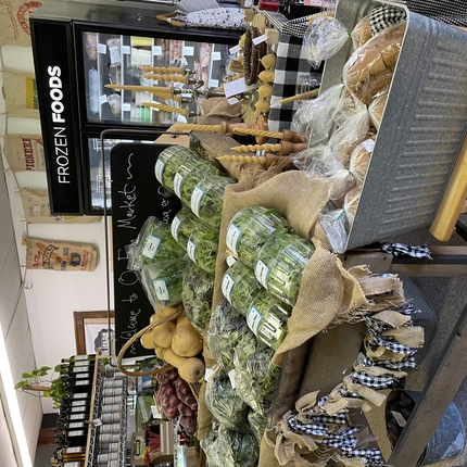 Una parada de verdures dins d'una botiga, amb diverses verdures, carbassa, pa envasat en contenidors d'alumini
