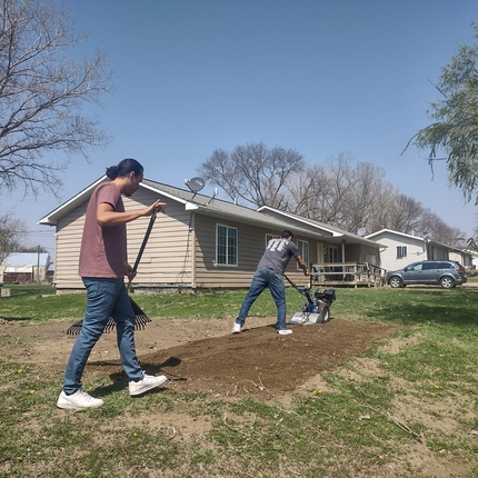 dos homes, un amb camisa marró i texans i l'altre amb camisa grisa i texans treballant per conrear un jardí.