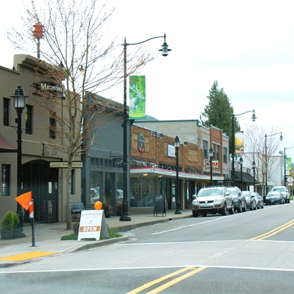 Store buildings on the left with cars parked along a main street.