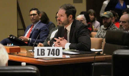 Home amb vestit assegut darrere d'un escriptori de fusta amb un rètol a l'escriptori que diu "LB 740"