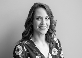 Woman with wavy brown hair smiling at the camera, wearing a dark shirt with flower print