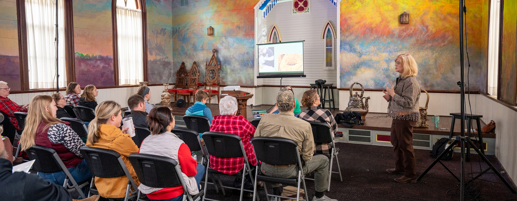 White female with blonde hair speaks to a sitting audience in a colorful church.