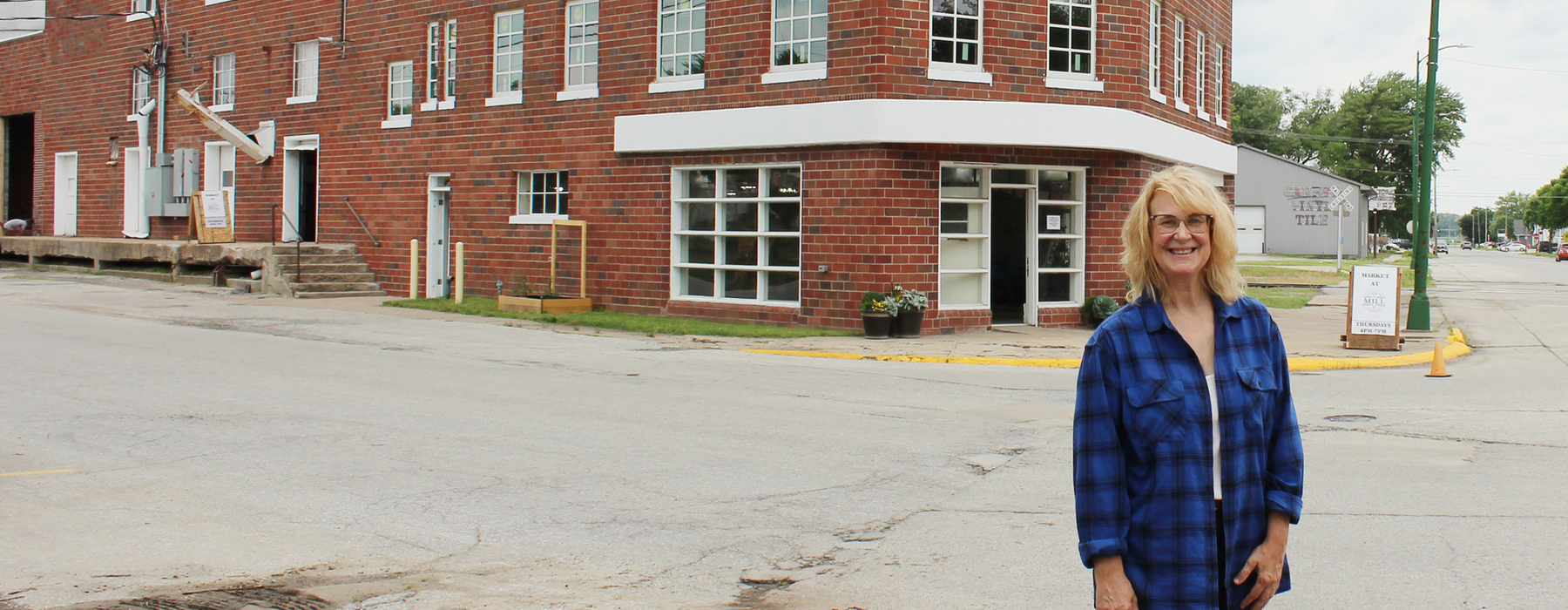 White woman with blonde shoulder-length hair stands on a small town street in front of brick corner building